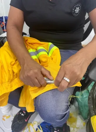 Costureira fazendo o acabamento de uma peça amarela com faixa refletiva
