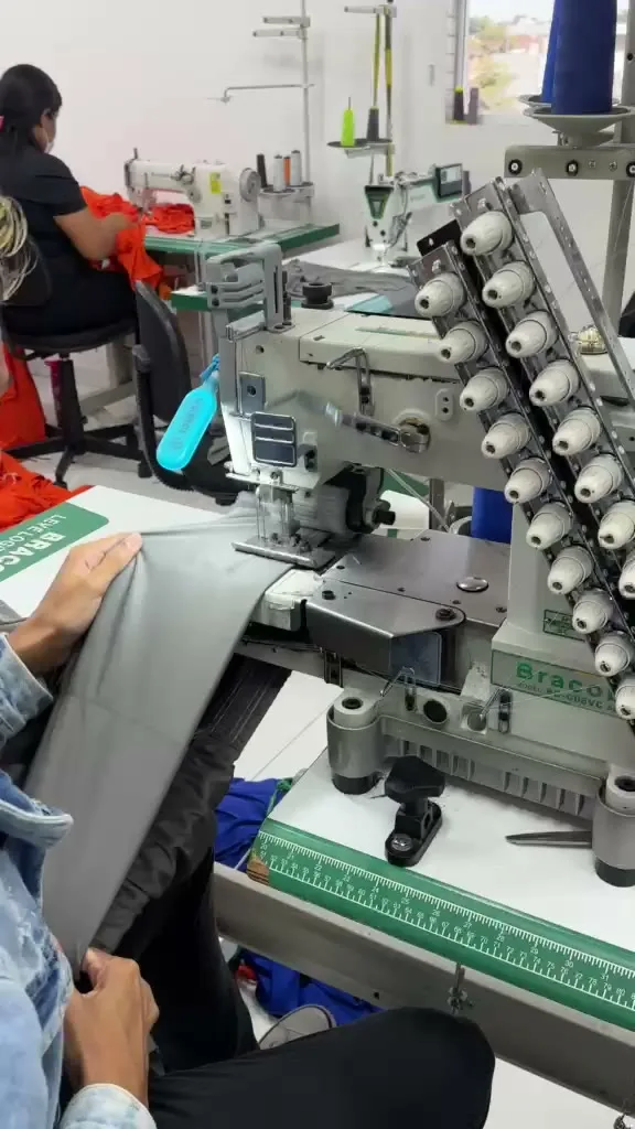 Máquina de costura industrial de várias agulhas costurando uma peça em malha cinza